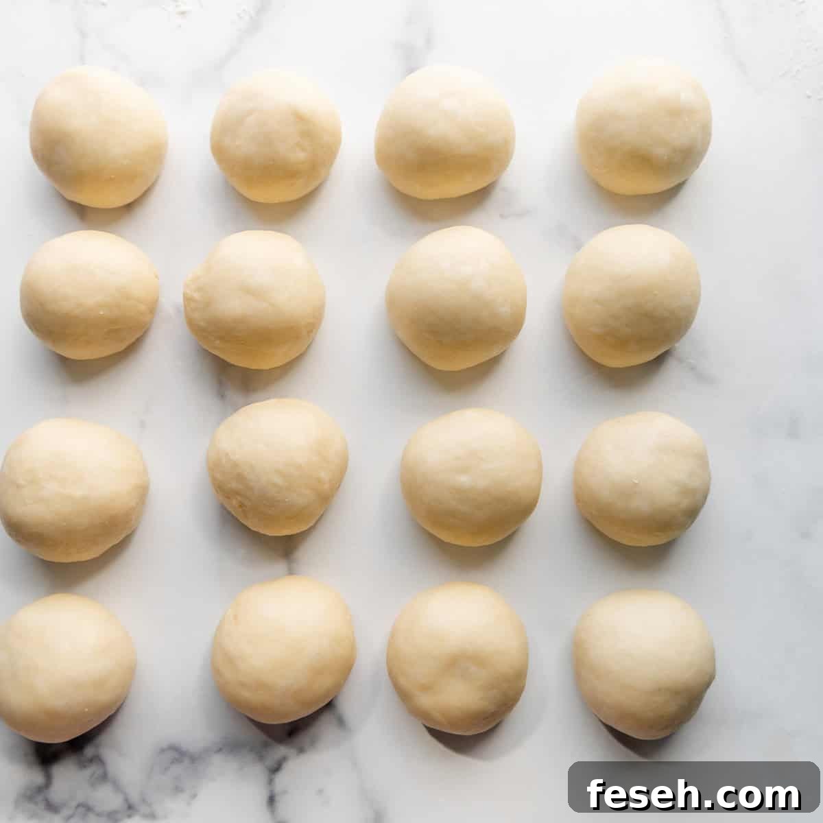 Fifteen neatly aligned balls of dough are placed on a marble surface, ready for baking or cooking.