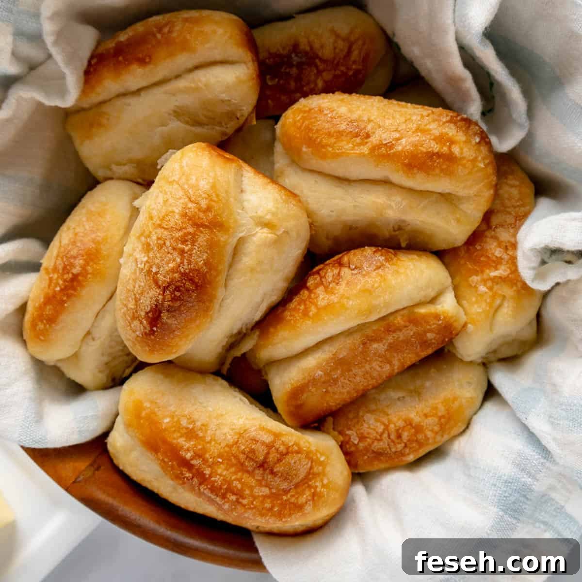 A basket filled with freshly baked golden brown dinner rolls on a cloth-lined surface.