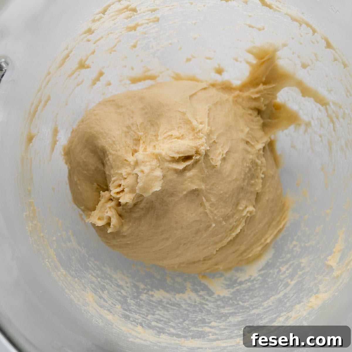 A ball of dough in a clear glass mixing bowl.