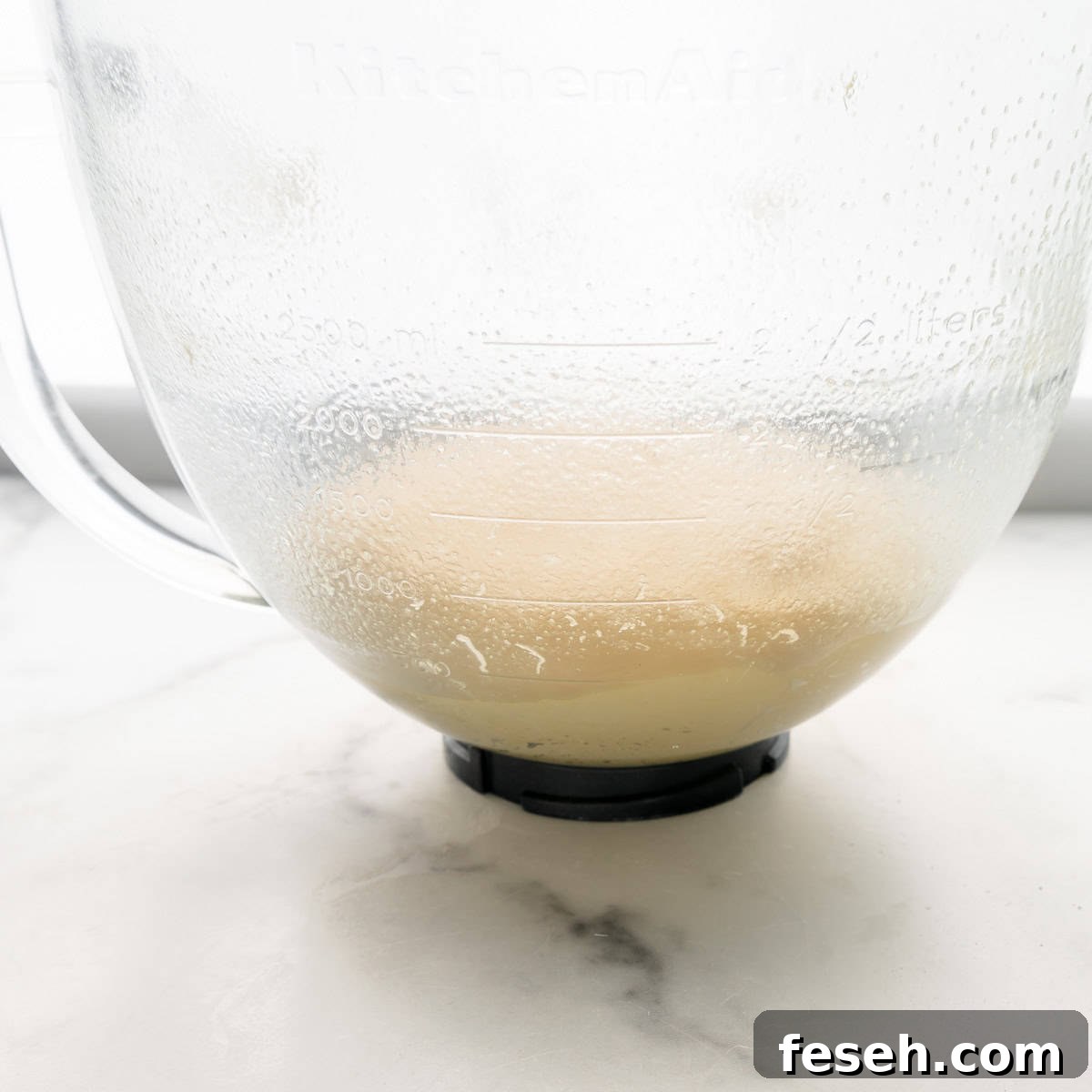 A transparent mixing bowl with dough on a white marble surface.