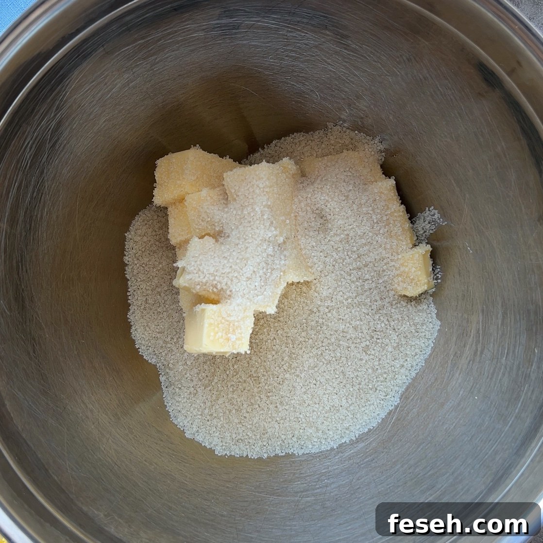 A stainless steel mixing bowl containing cubed butter and granulated sugar, ready to create the perfect Fruit Pizza base.