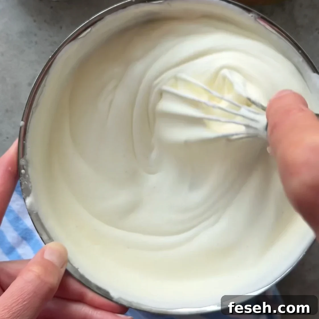 A person whisking thick, white mascarpone cream in a metal bowl.