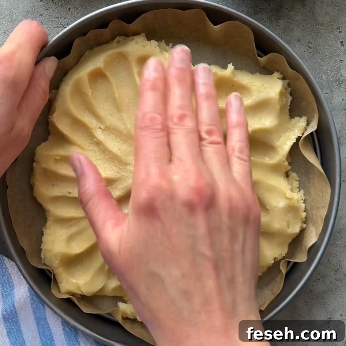 A person presses dough evenly into a parchment-lined round baking pan preparing the base for a delicious Fruit Pizza.