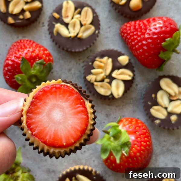 A hand holds a chocolate cup topped with a sliced strawberry, reminiscent of a strawberry Snickers treat.