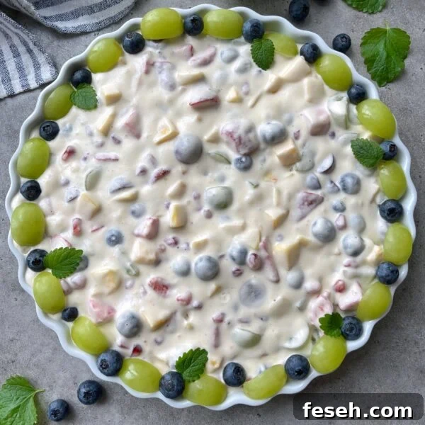 A round dish filled with creamy fruit salad topped with green grapes and blueberries.