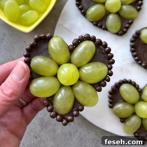 A hand holds a Grape Chocolate Heart decorated with green grapes.