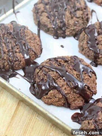 Chocolate almond flour cookies drizzled with chocolate on a piece of parchment paper on a baking sheet.