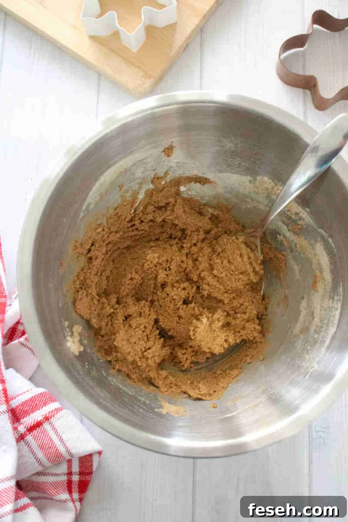 Raw cookie batter in a steel bowl with a spoon in it.