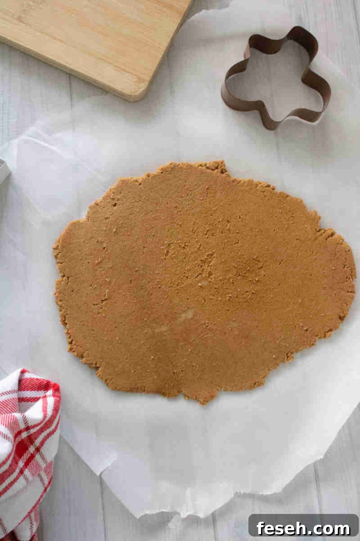 Raw cookie dough rolled out on parchment paper with a linen and cookie cutter next to it.