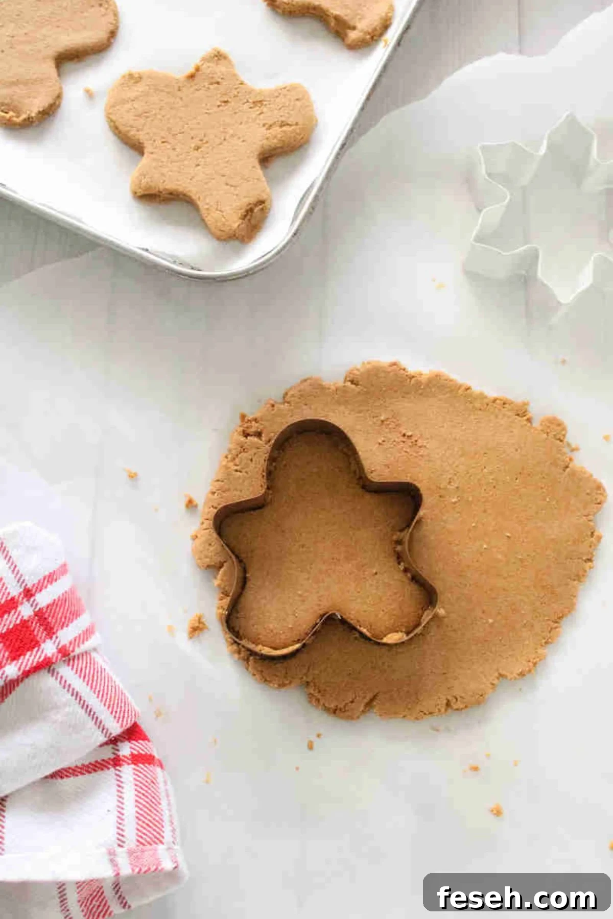 Raw cookie batter rolled on parchment paper with a gingerbread cookie cutter in the dough.