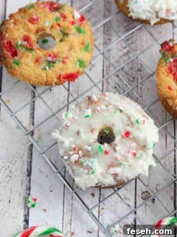 Frosted peppermint donut topped with candy canes on a cooling rack with other un-frosted donuts.