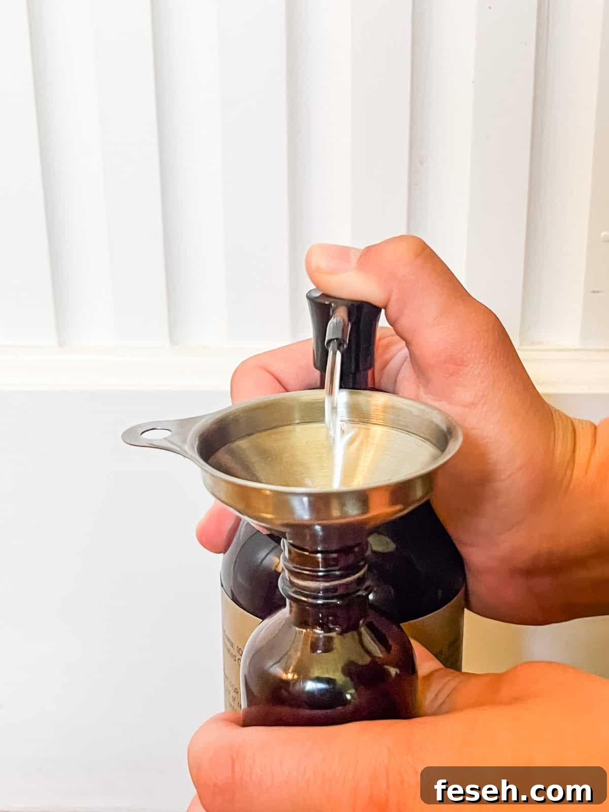 Squirting carrier oil into a glass bottle with a small funnel.