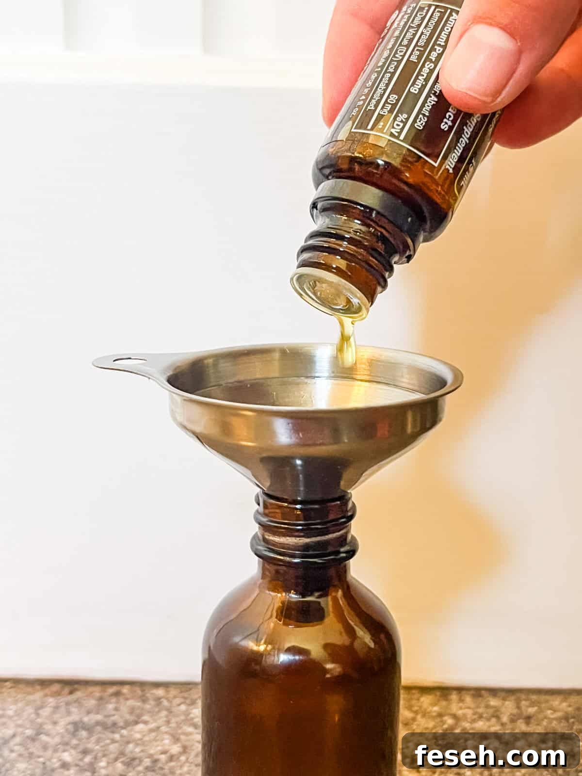 Dropping essential oils into a glass bottle with a small funnel.