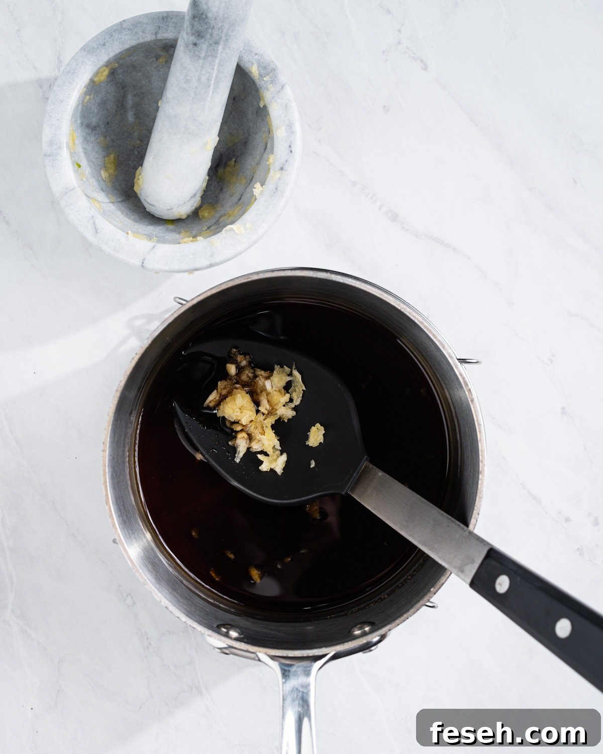 All of the eel sauce ingredients in a pot. Mortar and pestle with mashed garlic on the side.