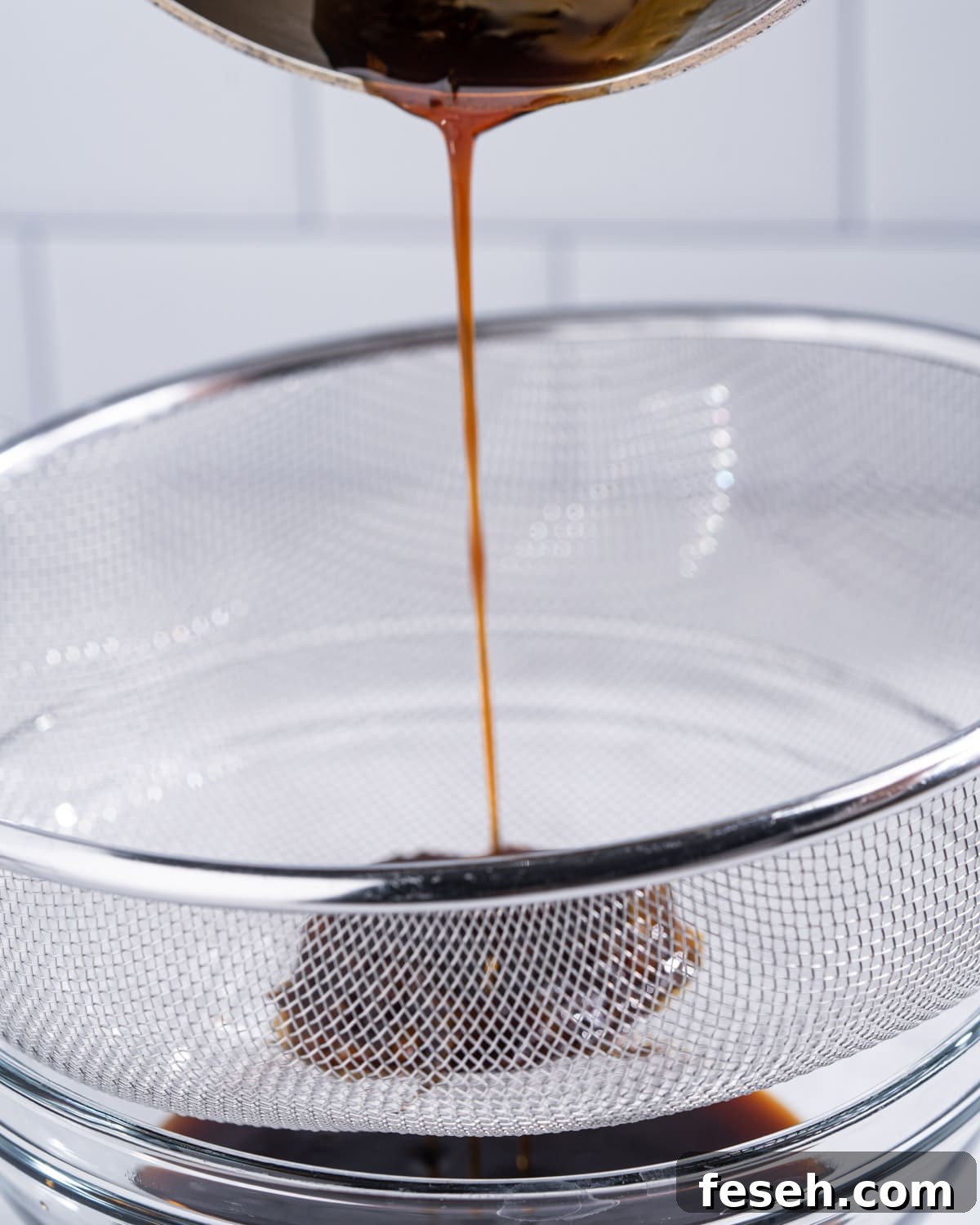Pot of unagi eel sauce being poured through a fine mesh strainer.