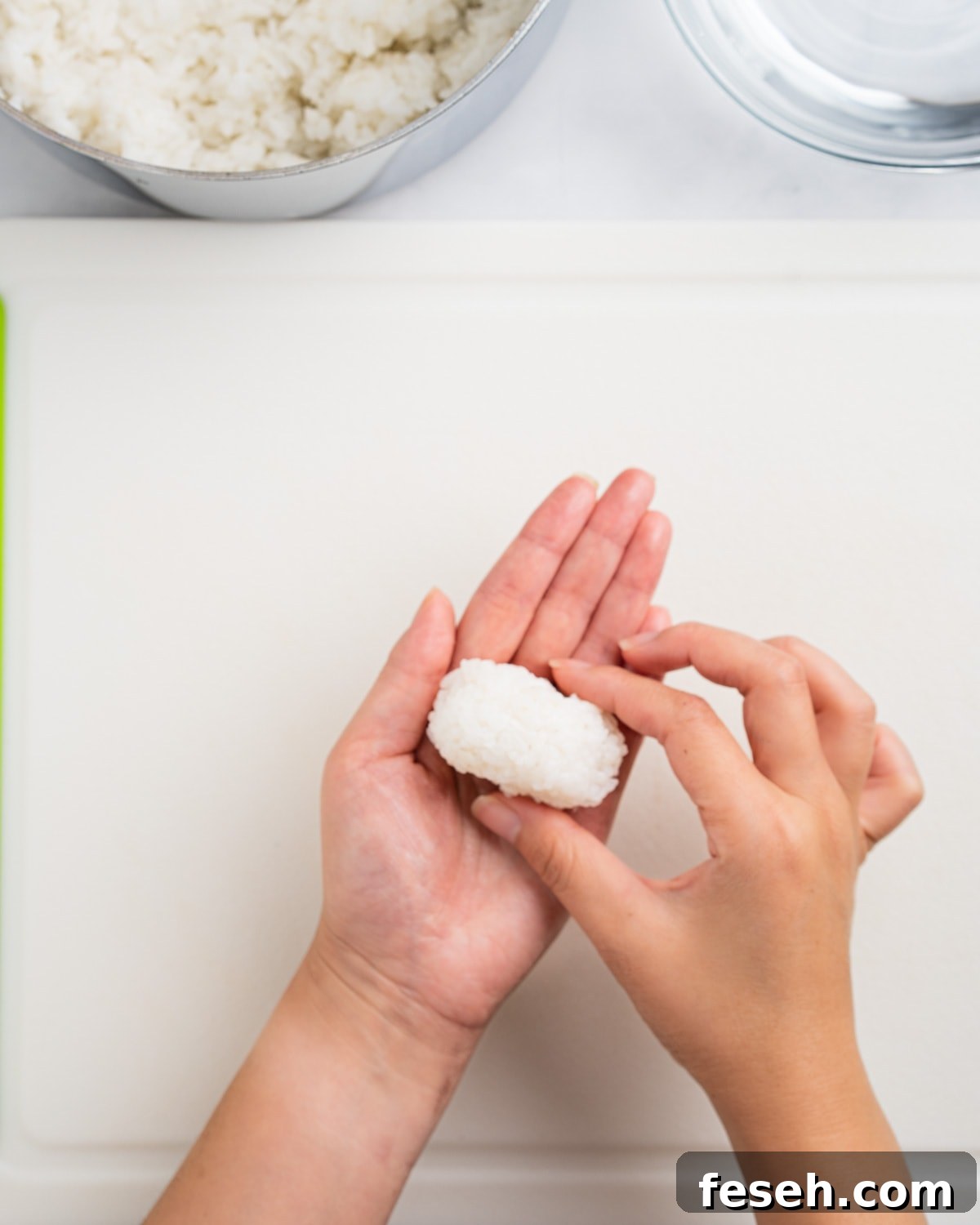 Hands shaping a small mound of rice for unagi sushi. Rice and water bowl on the side.