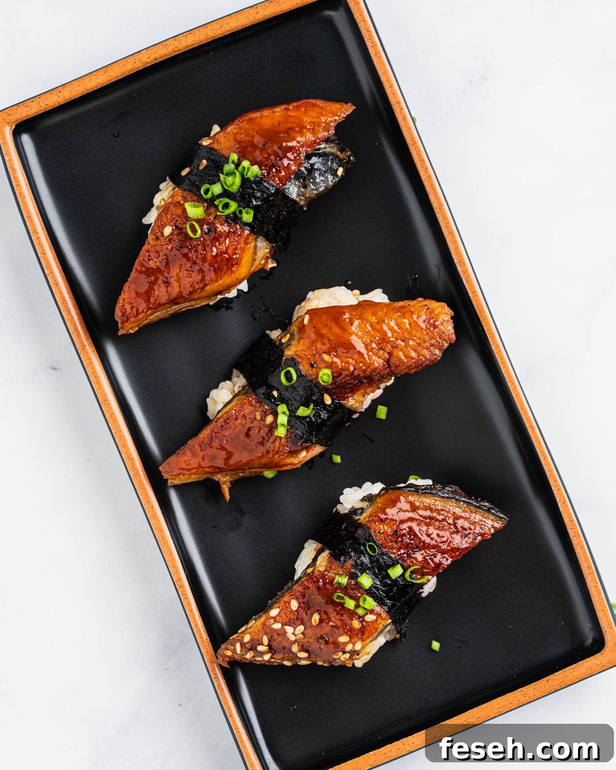 3 Grilled bbq Unagi sushi on a black plate.