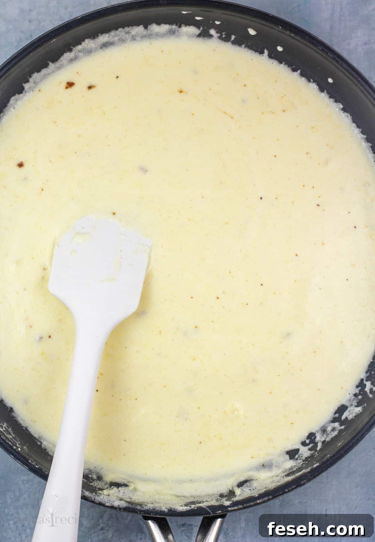 alfredo sauce in skillet with white rubber spatula