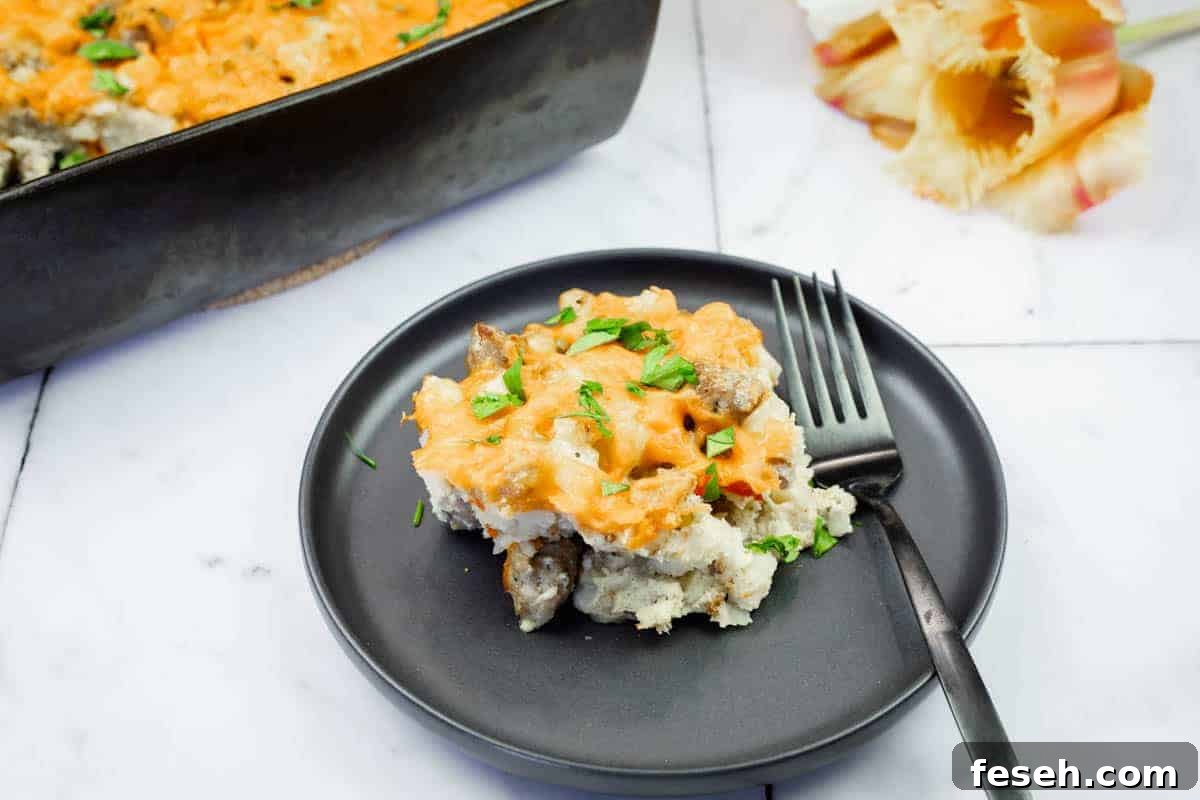 17 Pantry-Friendly Nanna Casseroles That Taste Homemade and Luxurious 6 A serving of Sausage-Hash Brown Breakfast Casserole on a black plate with a fork, next to a baking dish and pasta shells on a marble surface.