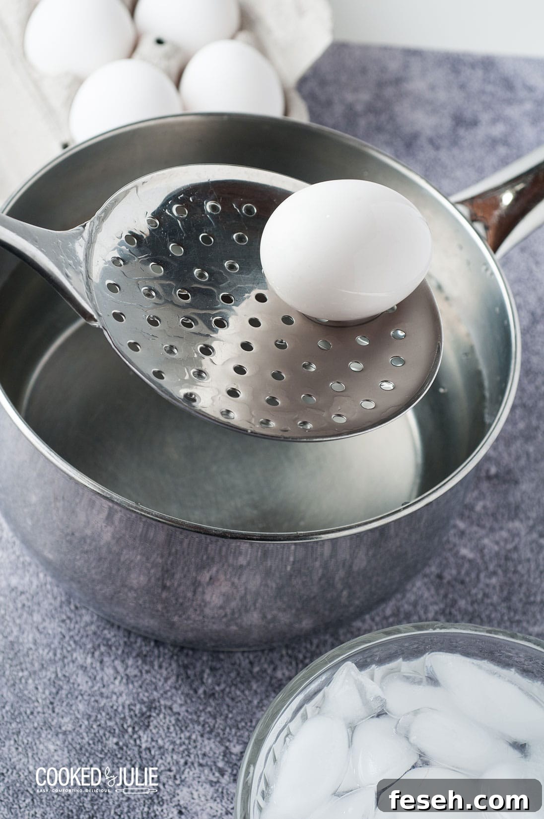 a straining spoon lifting a white egg out of a metal saucepan