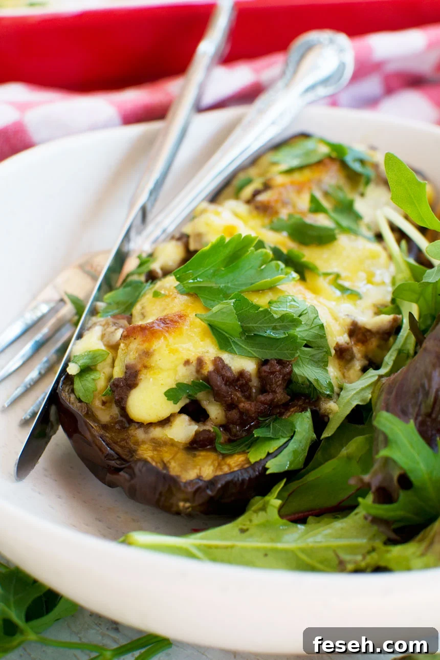 A close up of a white plate of Greek stuffed eggplant or papoutsakia served with a green salad