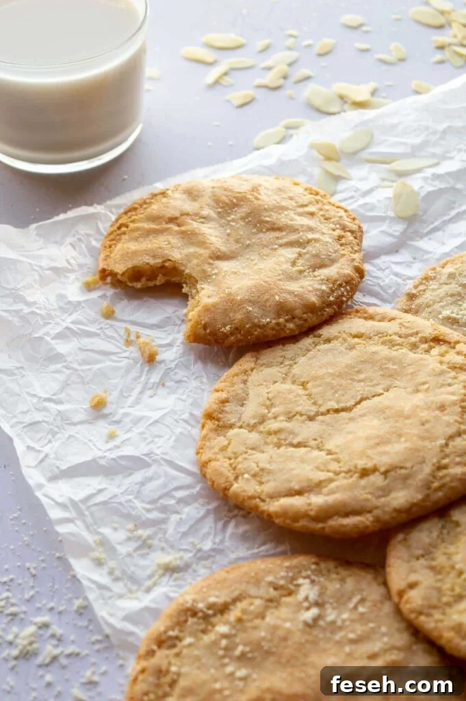 A glass of milk and several golden cookies on a white paper background.