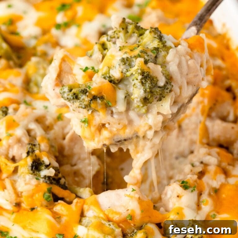 A close-up of Cheesy Chicken Broccoli and Rice Casserole, with gooey melted cheese stretching as a spoon lifts out a serving.