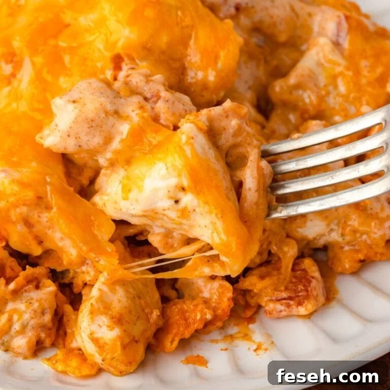 A fork digging into a cheesy Doritos casserole on a white plate.