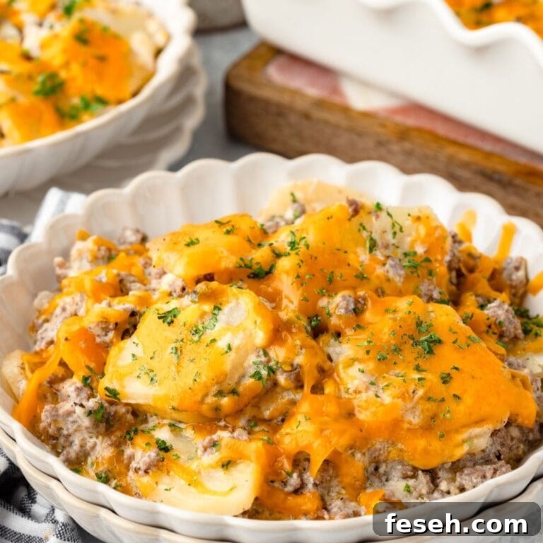 Close-up of a white dish with cheesy hamburger potato casserole, parsley garnish, and background dishes.