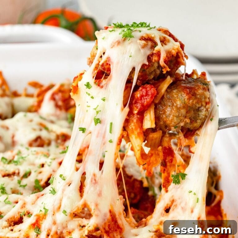 A close-up of a cheese meatball casserole being lifted from a dish, showing melted mozzarella cheese stretching and topped with tomato sauce and chopped parsley.