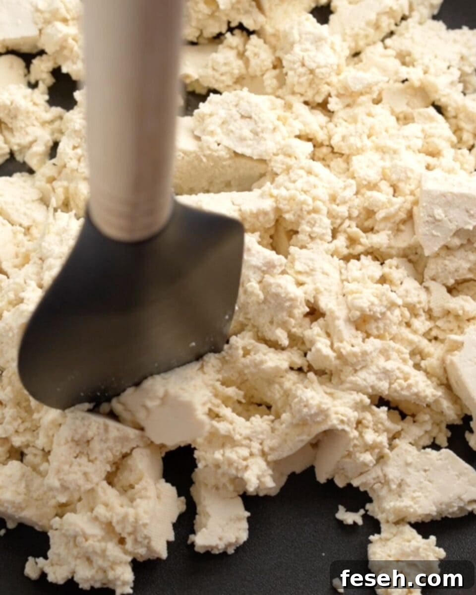 Tofu cooking in a pan with a spatula breaking up big chunks.