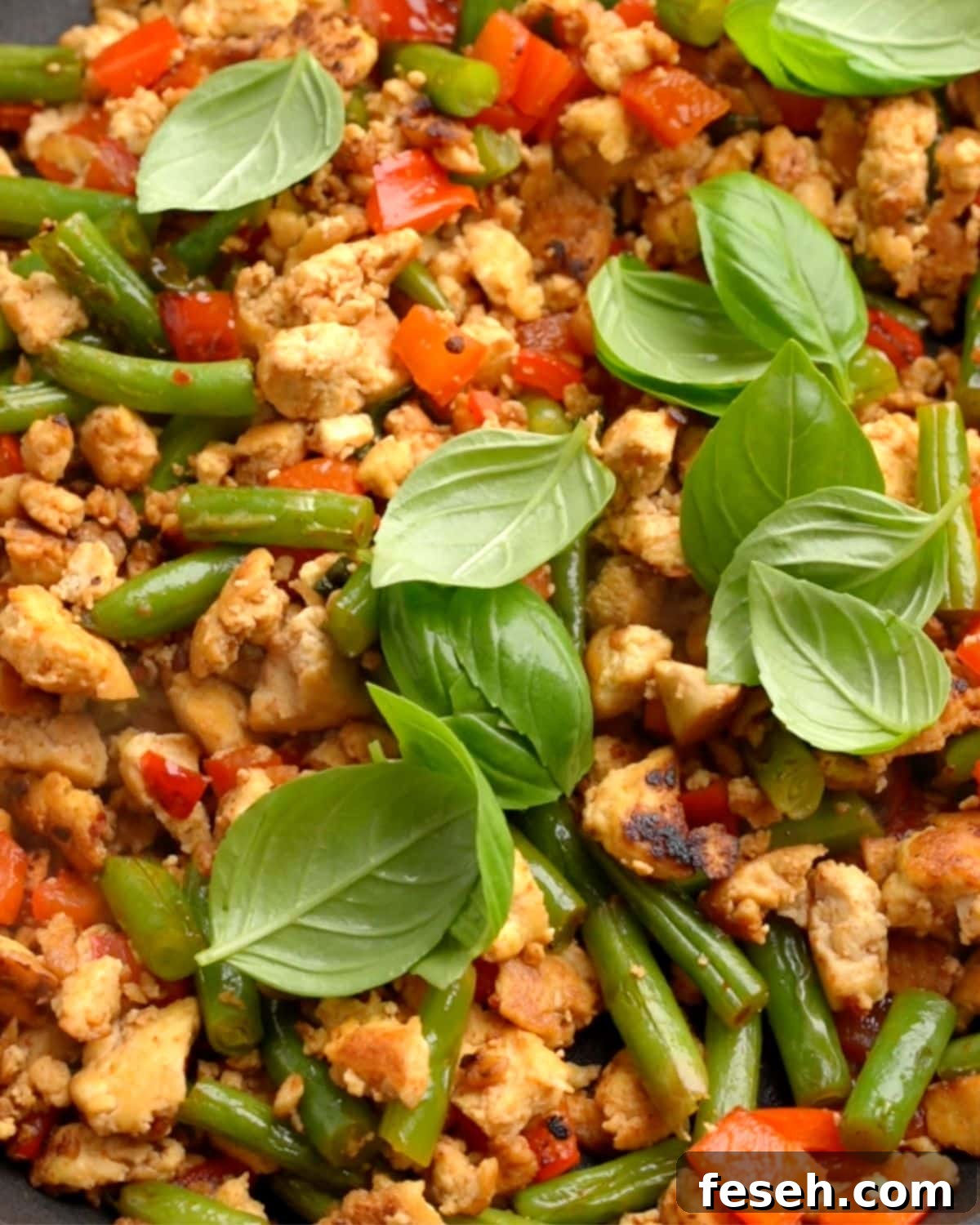 Stir fried pad kra pao with tofu in a pan with fresh basil on top.