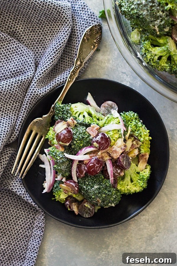 overhead: a small black bowl of broccoli salad with grapes with a fork