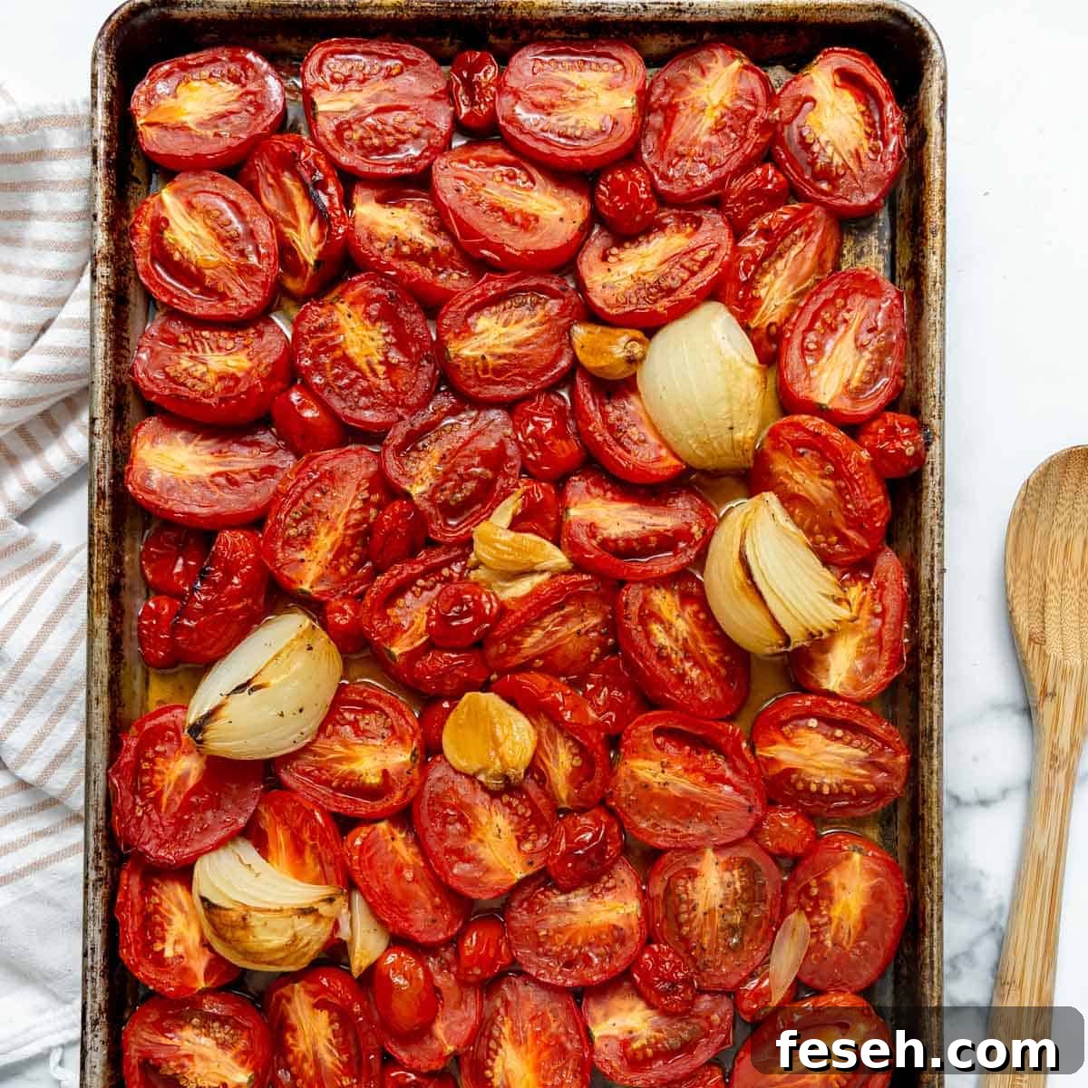 Halved tomatoes, onion wedges, and garlic cloves arranged on a baking sheet, roasted.