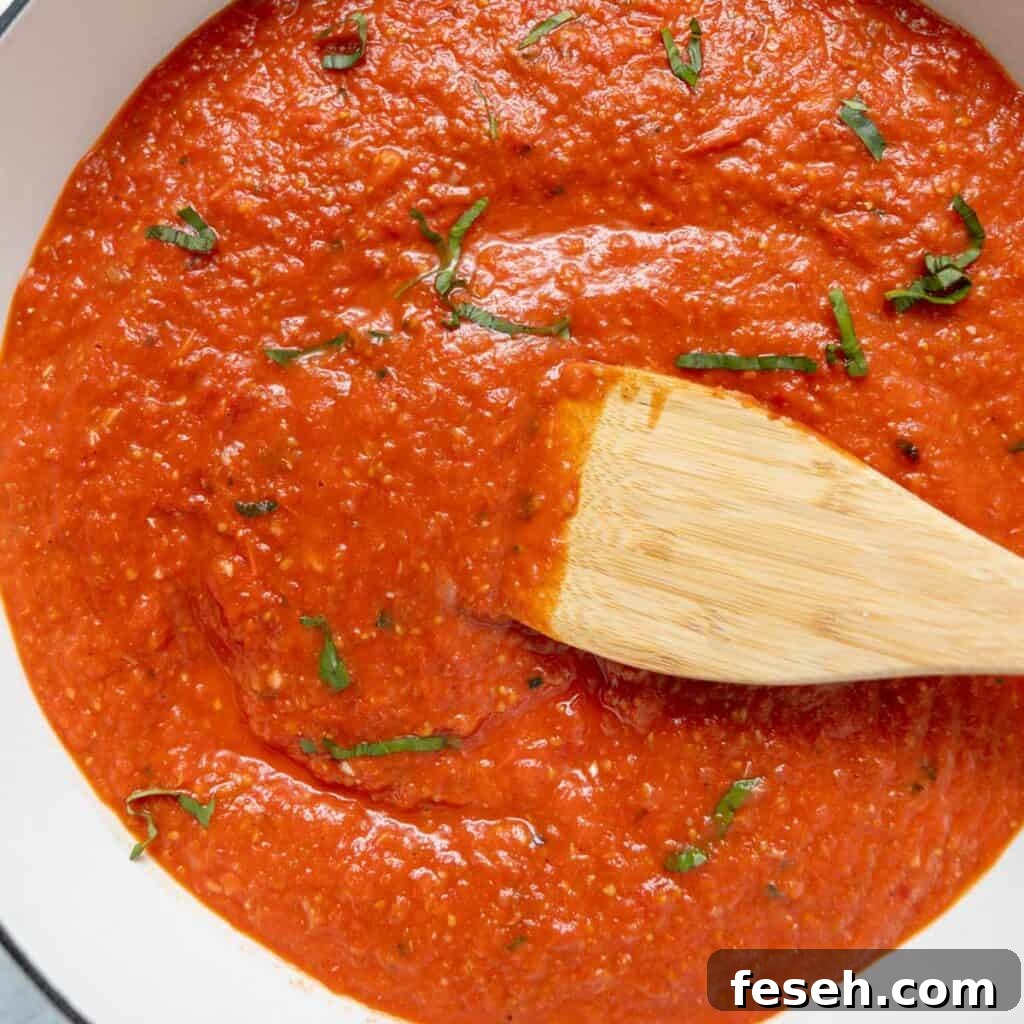Tomato sauce with chopped basil, stirred with a wooden spatula in a white pot.