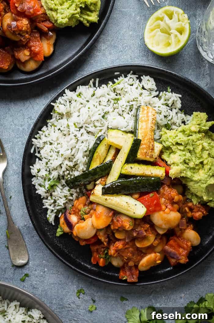 Close up of a black plate full of chilli, coriander rice, guacamole and roasted courgette.