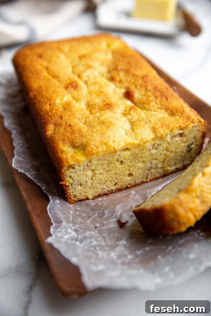 A loaf of gluten free banana bread on a wood serving board, with a slice cut out.
