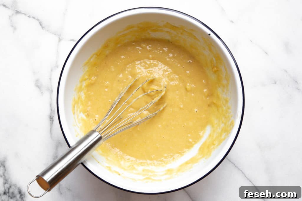The banana bread batter in a bowl with a whisk.