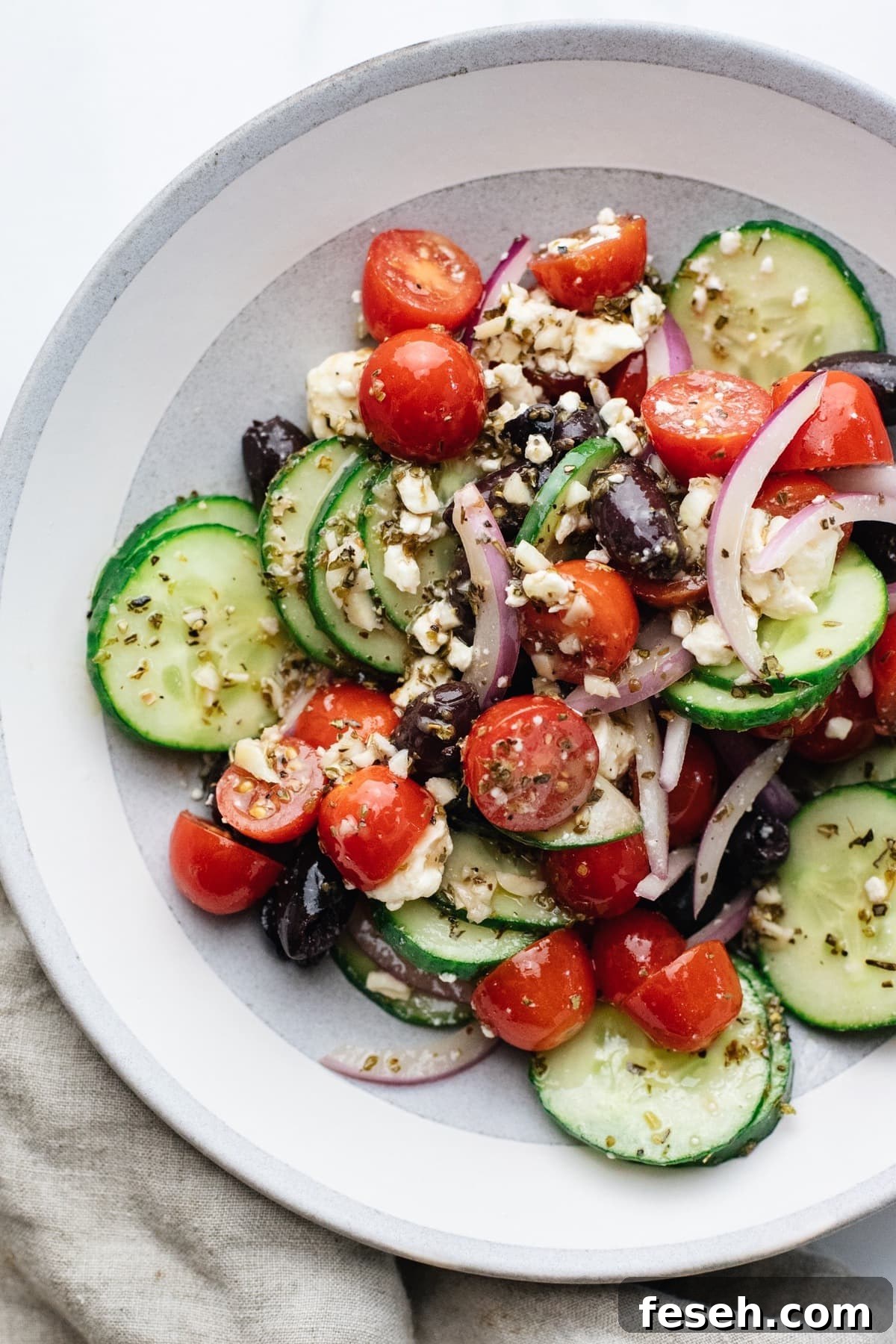 A ceramic bowl with cucumbers and tomatoes tossed with dressing.