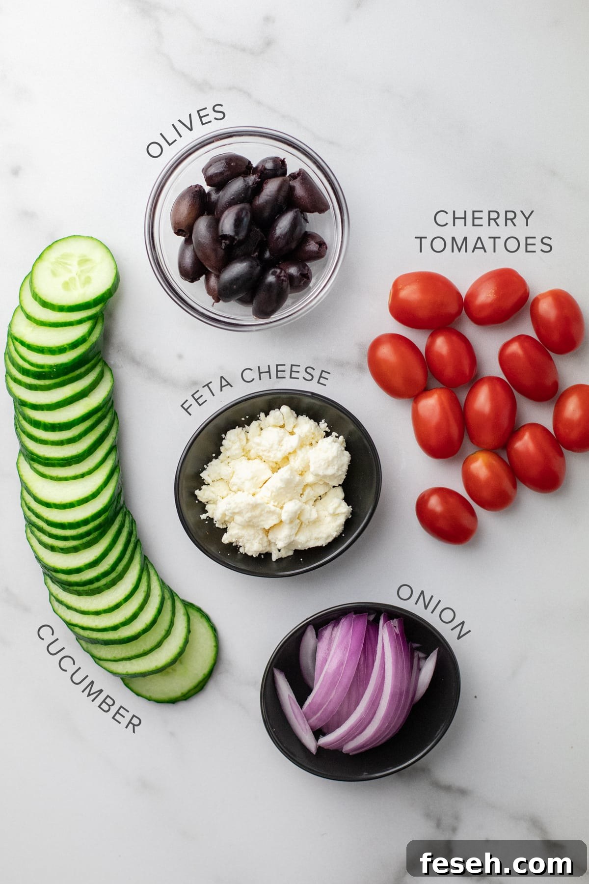Vegetables for a salad arranged on a white counter.