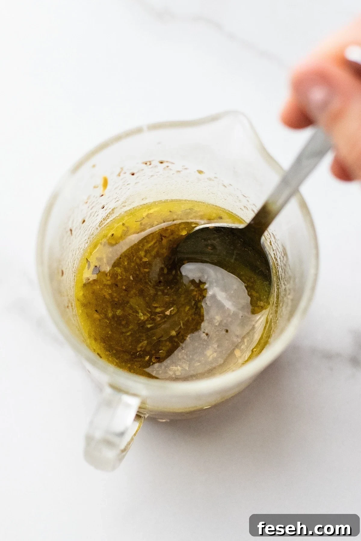 A spoon stirring homemade salad dressing in a clear glass jar.