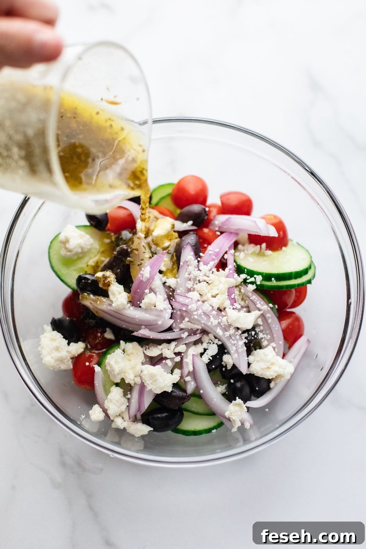 Dressing being poured over a greek salad.
