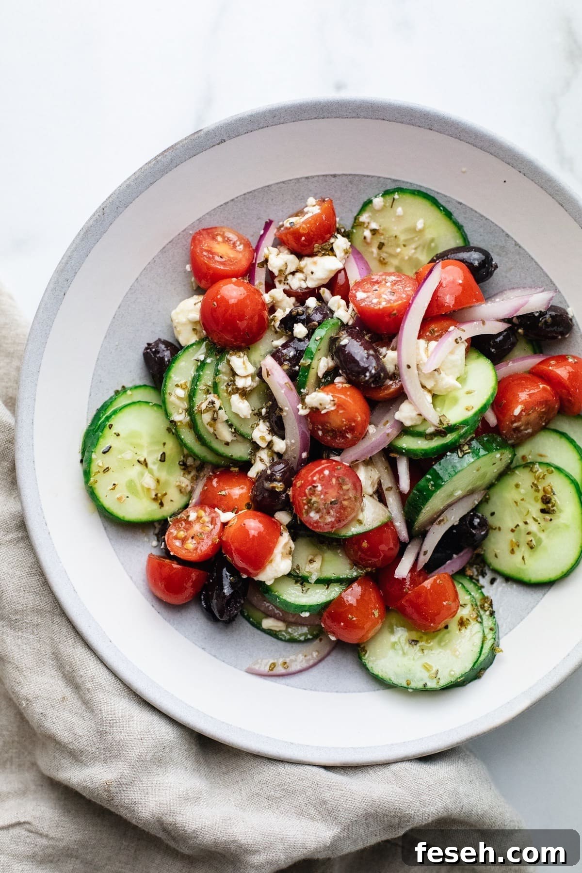 A ceramic bowl with sliced tomatoes and cucumbers and a grey napkin on the side.