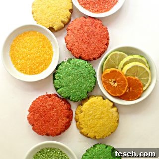 sugar cookies on white background with white bowls of colored sugar and sliced citrus fruit