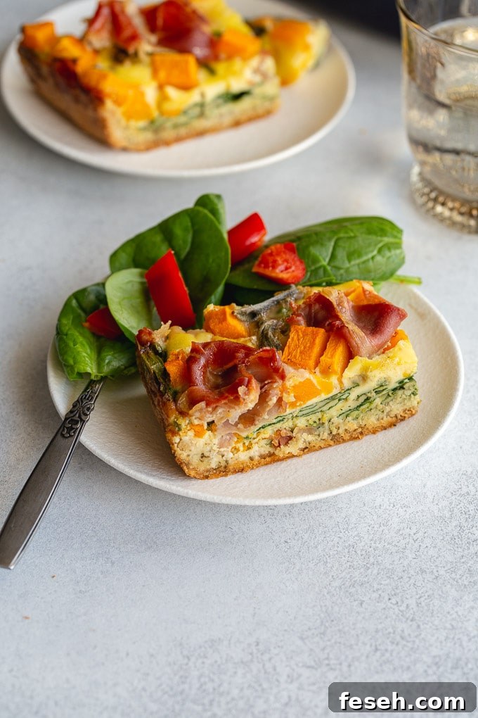 Side view of a slice of quiche on a white plate with a salad.