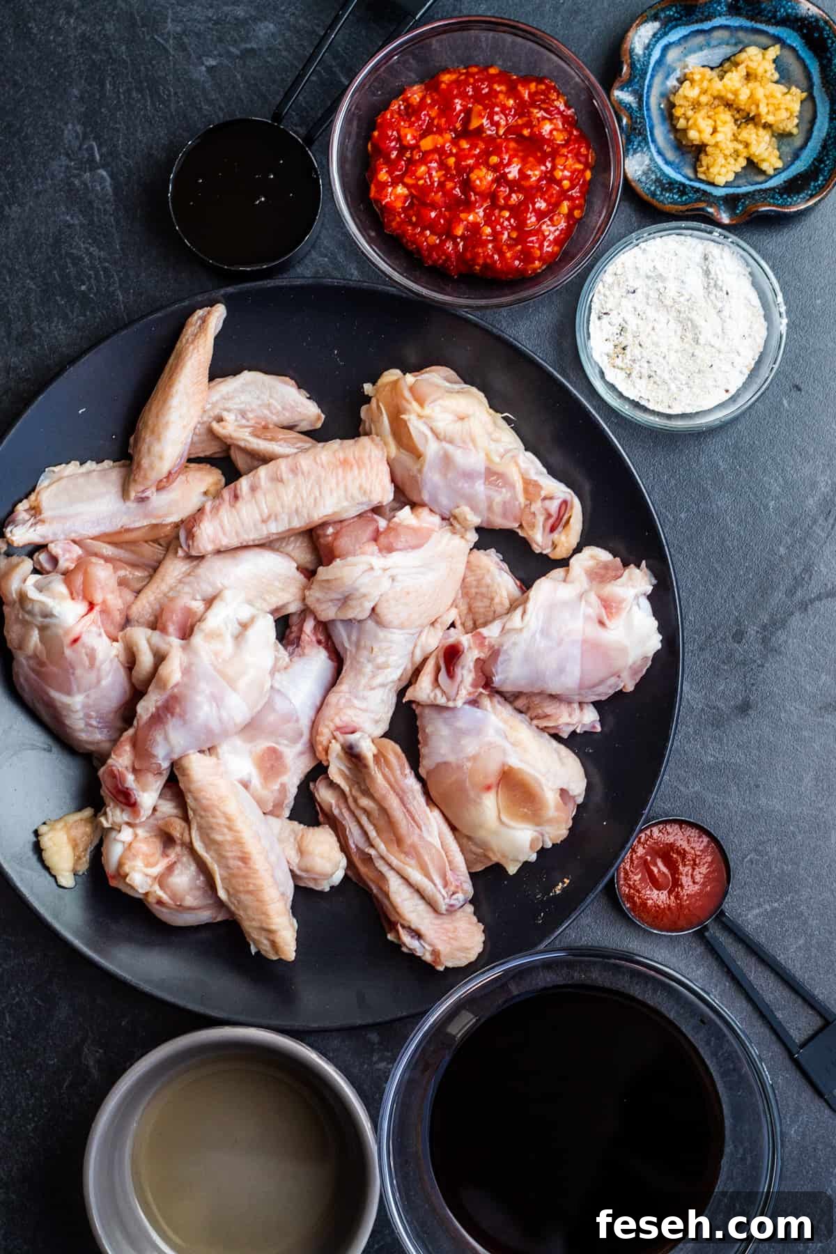 Overhead shot of chicken wing ingredients in small bowls on dark background.