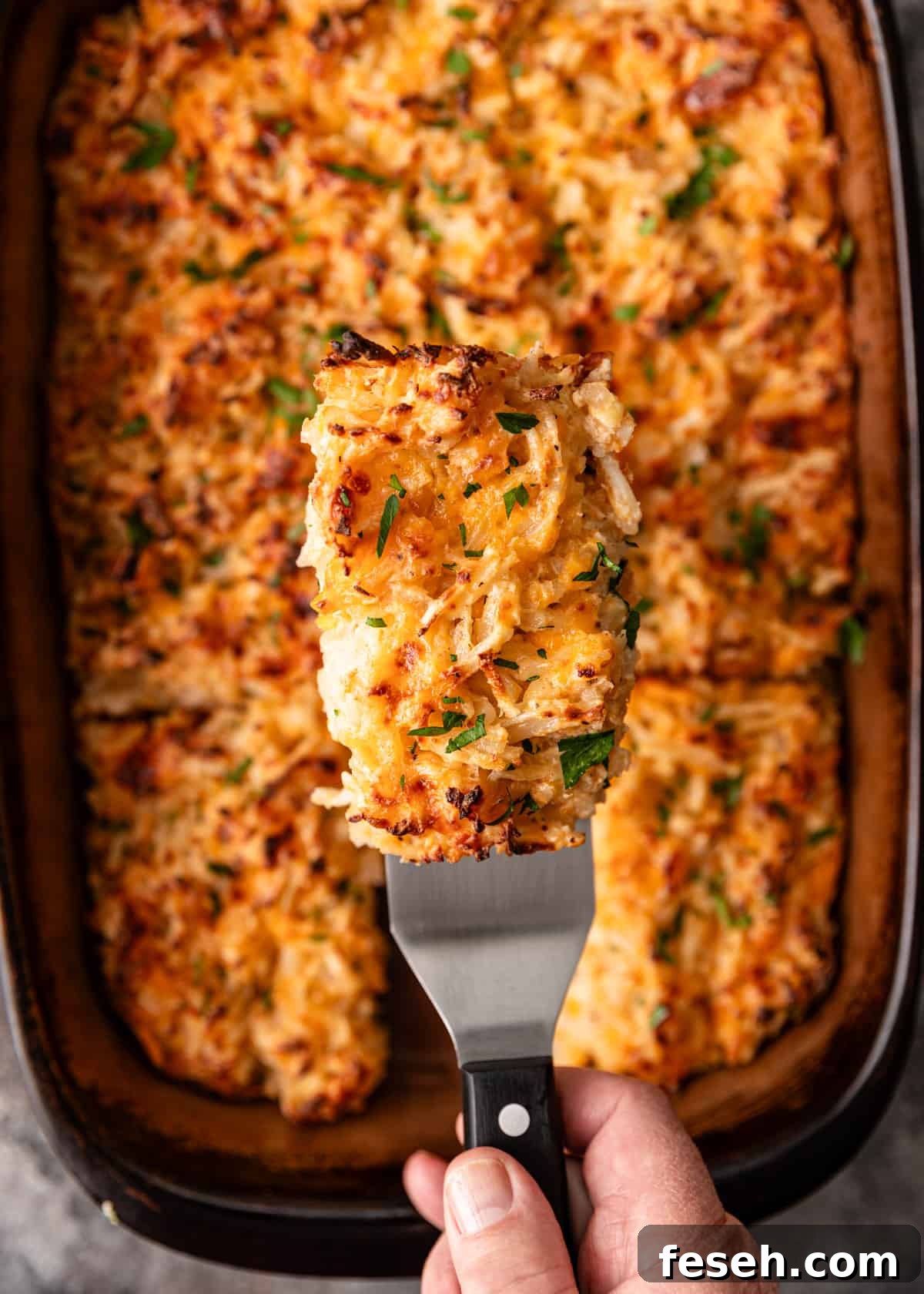 Southern Hashbrown Casserole Recipe for Comforting Family Dinners 8 overhead: lifting a slice of hashbrown casserole out of a casserole dish
