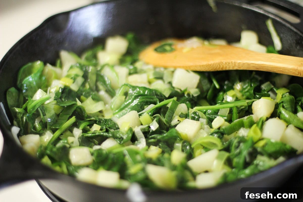 Cast iron skillet with potatoes, spinach, and leek sautéing.