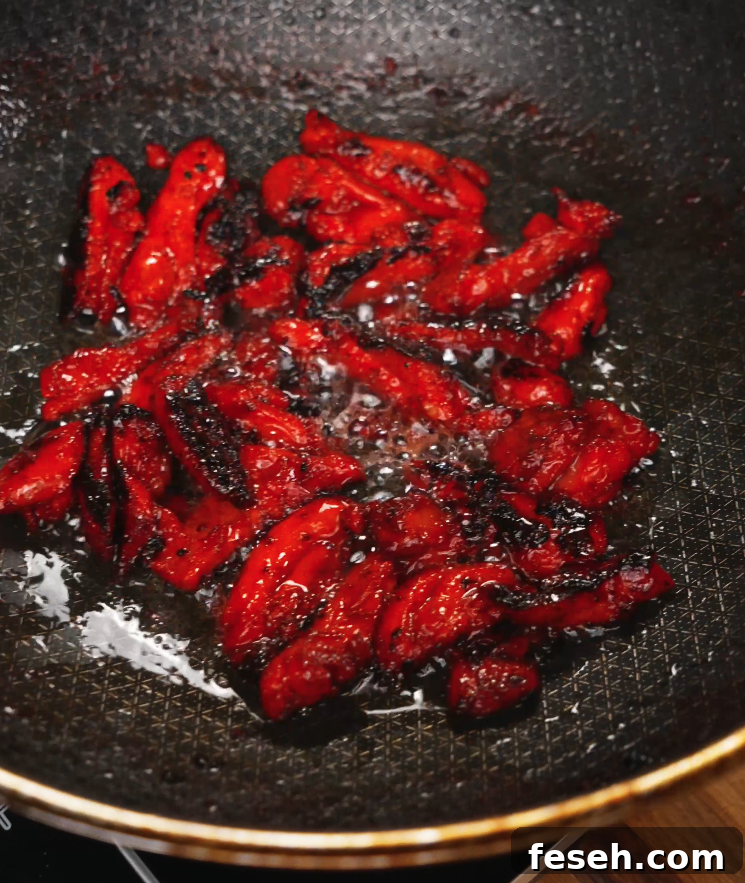 Strips of marinated Chicken Tocino sizzling in a pan, developing charred edges and a sticky glaze. This caramelization is essential for bringing out the sweet and smoky flavors of the dish.