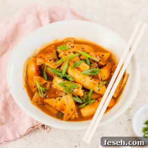 a bowl of vegan tteokbokki next to a small bowl of sesame seeds with chopsticks on the side